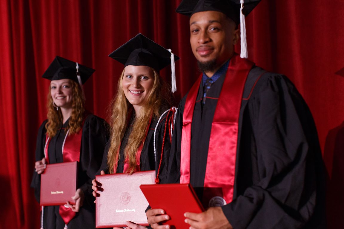 three new IUK graduates standing, holding their diplomas